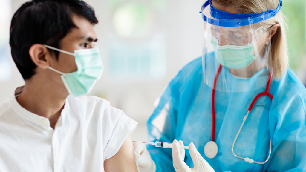 Nurse wearing PPE injecting man with needle/vaccine.