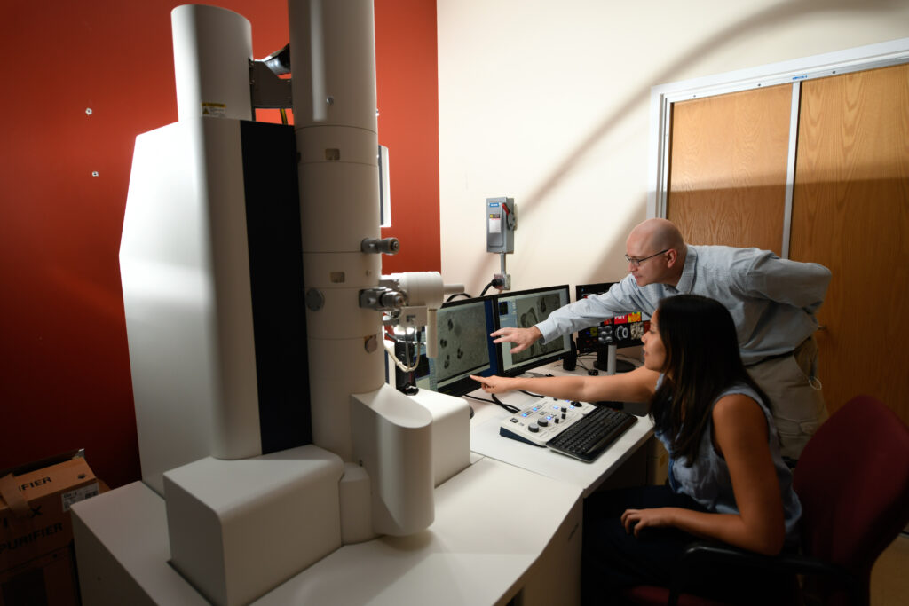 Dr. Bell working with woman in suite with Hitachi HT7800 EM. Woman is seated and Dr. Bell is pointing to computer screens with images. 